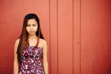 Portrait of beautiful girl on red concrete wallの写真素材