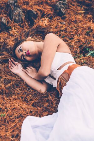 Portrait of beautiful wiccan girl in the forest. Beautiful woman in white dress laying on the ground in the forestの写真素材