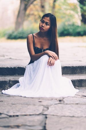 Beautiful girl in long white dress, daydreaming in the parkの写真素材