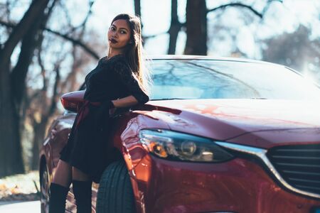 Young beautiful girl in black dress with the red sport carの写真素材