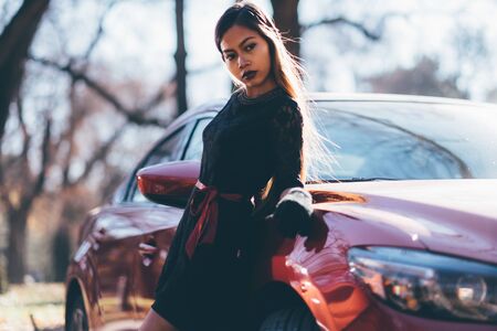 Young beautiful girl in black dress with the red sport carの写真素材