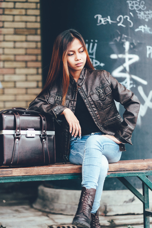 Gorgeous girl in leather jacket sitting on the bench with the leather bagの写真素材