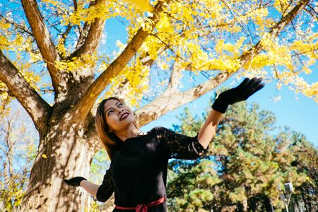 Happy young woman in park on sunny autumn day, smiling. Cheerful beautiful girl in black retro dress autumn fashion styleの写真素材