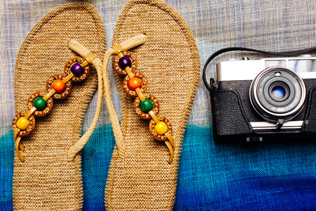 Flat lay of summer object with camera and slippers on top of the bag as backgroundの写真素材