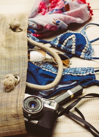 Flat lay of summer fashion with blue bikini swimsuit inside the bag, and other girl accessories on white wooden  backgroundの写真素材
