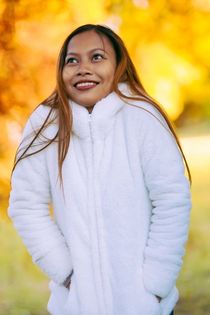 Portrait of a happy young beautiful woman in autumn season in white woolen jacket outdoor with colorful autumn background.の写真素材