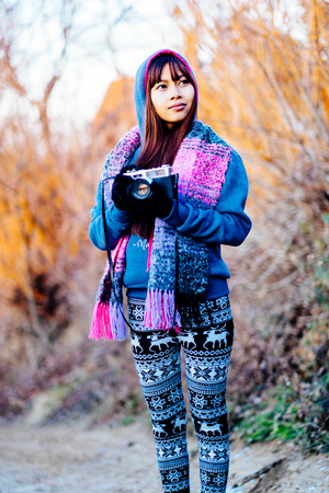 Young female photographer in cold weather wearing sweater and colorful scarf during afternoon sunset...