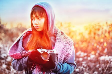 Young female photographer in cold weather wearing sweater and colorful scarf during afternoon sunset outsideの写真素材