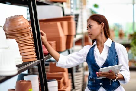 Young pretty Asian woman agronomist with tablet working in greenhouse checking the storage inventory.の写真素材