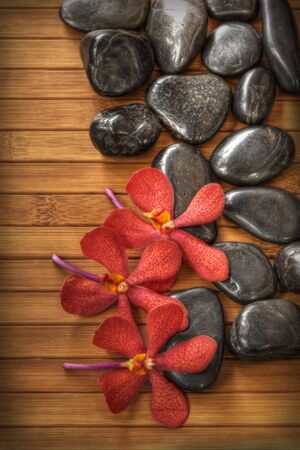 Beautiful red orchid and black stone on bamboo matの写真素材