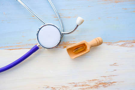 Blue stethoscope with fish oil capsules on light blue and white vintage wooden table background.