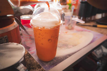 Making of Thai orange traditional milk tea with milk foam . street food ready for drinkの写真素材