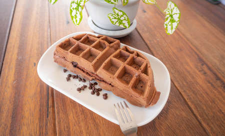Fresh chocolate waffles with chocolate chip on a white plate on wooden table cafe background