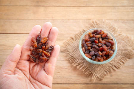 Raisin on hand with raisin in bowl and wooden on background. Choose a good raisin concept.の写真素材