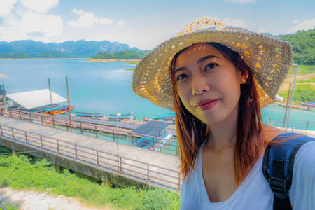 Happy young woman tourist in asian hat on lake and mountain vacation smiling at camera taking photo on summer holiday in Thailand.の写真素材