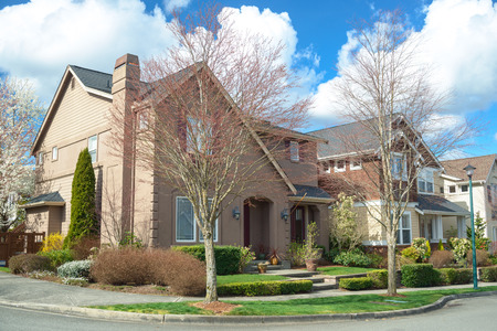 Beautiful american houses on the corner of the street. There is porch visible, green lawn, nice landscaping, sidewalk and spring trees.の写真素材