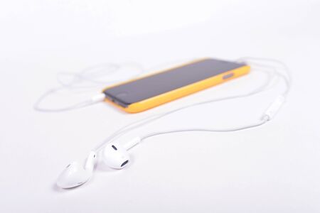 white headphones connected to black phone in yellow case lying on a white backgroundの写真素材