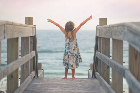 Little girl with open arms near the oceanの写真素材
