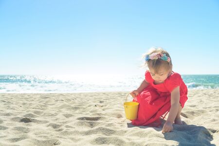 Little blond girl in red dress on the beachの写真素材