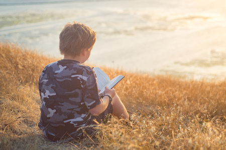Boy reading book outside at sunsetの写真素材