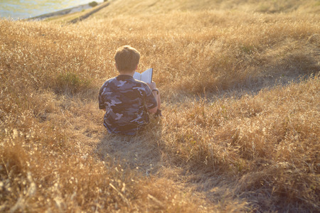 Boy reading book outside at sunsetの写真素材