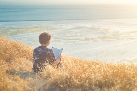Boy reading book outside at sunset