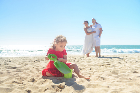 Girl digging sand on beach with parents in backgroundの写真素材