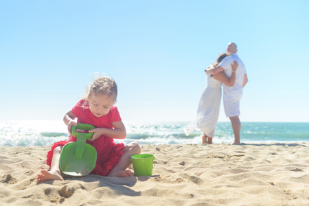 Girl digging sand on beach with parents in backgroundの写真素材