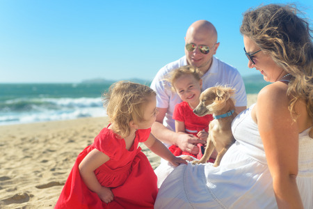 Family with sisters in red dress and dog on the beachの写真素材