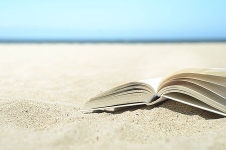 Close up of open book on the beach on warm yellow sand with ocean in the distance. Turn the page and relax.の写真素材