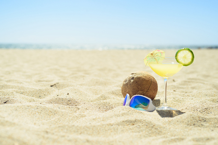 Sunglasses with cocktail glass and coconut on the beachの写真素材