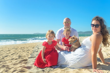 Family with sisters in red dress and dog on the beachの写真素材