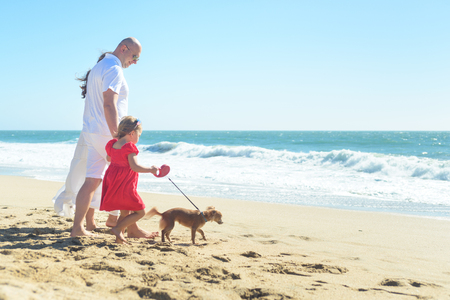 Young family with girl in red dress and dog on the beachの写真素材