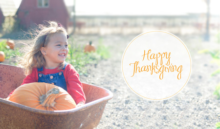 Happy smiling girl sitting inside wheelbarrow at field pumpkin patchの写真素材
