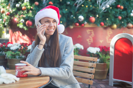 Smiling woman in Santa hat talking on her phone in cafe outsideの写真素材