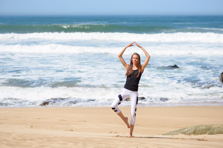 Smiling active young woman doing yoga on the beachの写真素材