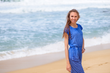 Beautiful smiling young girl in blue walking on the beach on vacationの写真素材
