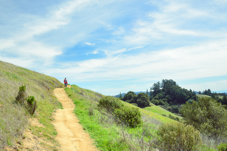 Hiker in red jacket with backpack on trail in beautiful landscapeの写真素材
