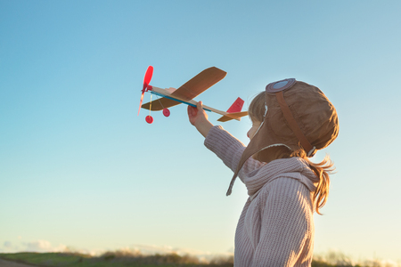 Girl in aviator hat playing pilot with toy plane outsideの写真素材
