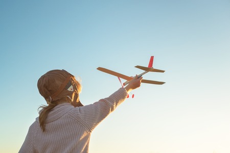 Girl in aviator hat playing pilot with toy plane outside