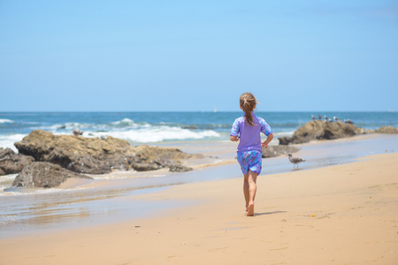 Happy girl running on the beach to the oceanの写真素材