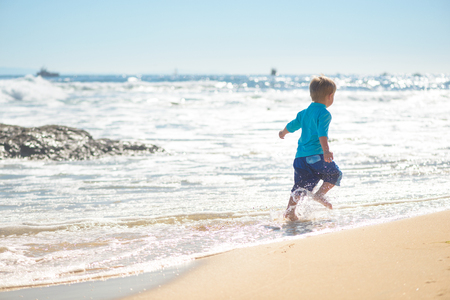 Happy boy running on the beach in the wavesの写真素材