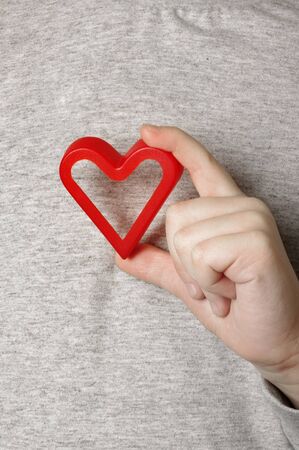 Child's hand with a red heart in the grey background  の写真素材