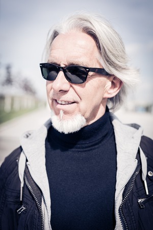 outdoor portrait of a modern senior man with long hair and beardの写真素材