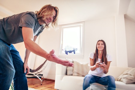 Young couple playing with a small quadrocopter drone at home in their living room.の写真素材