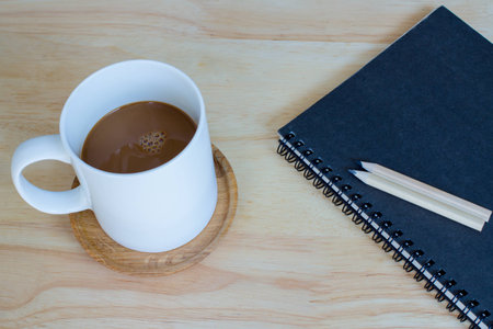 focus cup coffee on wood table and two pencil on  black note bookの写真素材