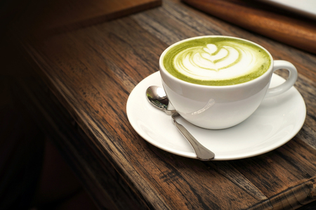 Hot green tea matcha latte on wooden table in the cafeの写真素材
