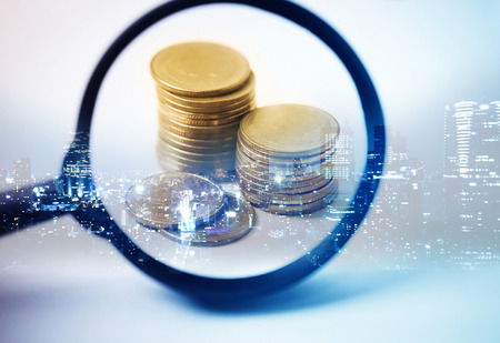 Double exposure of city and the magnifying glass focus at rows of coins for finance and banking conceptの写真素材