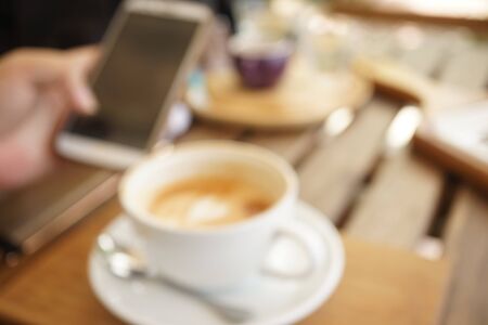 blur background of a cup of coffee and using smart phone on the wooden table in the coffee shopの写真素材
