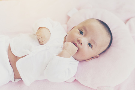 A baby boy wearing a white dress, lying on a bed of pink, do doubt.の写真素材